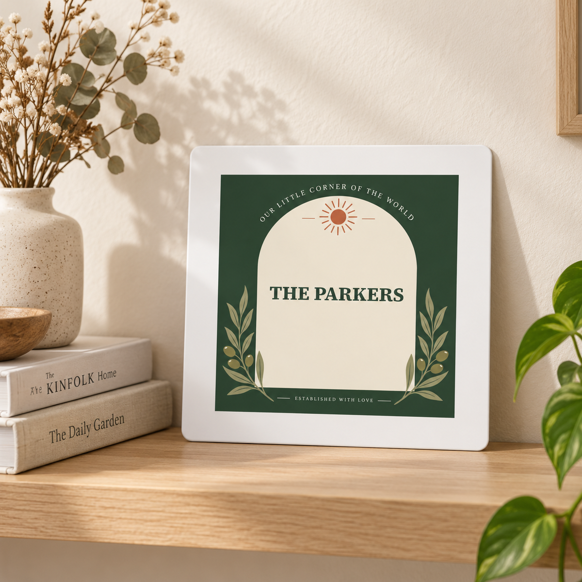 Lifestyle mockup of the personalized Olive Arch family name metal sign on an indoor oak shelf with neutral books and a ceramic vase.